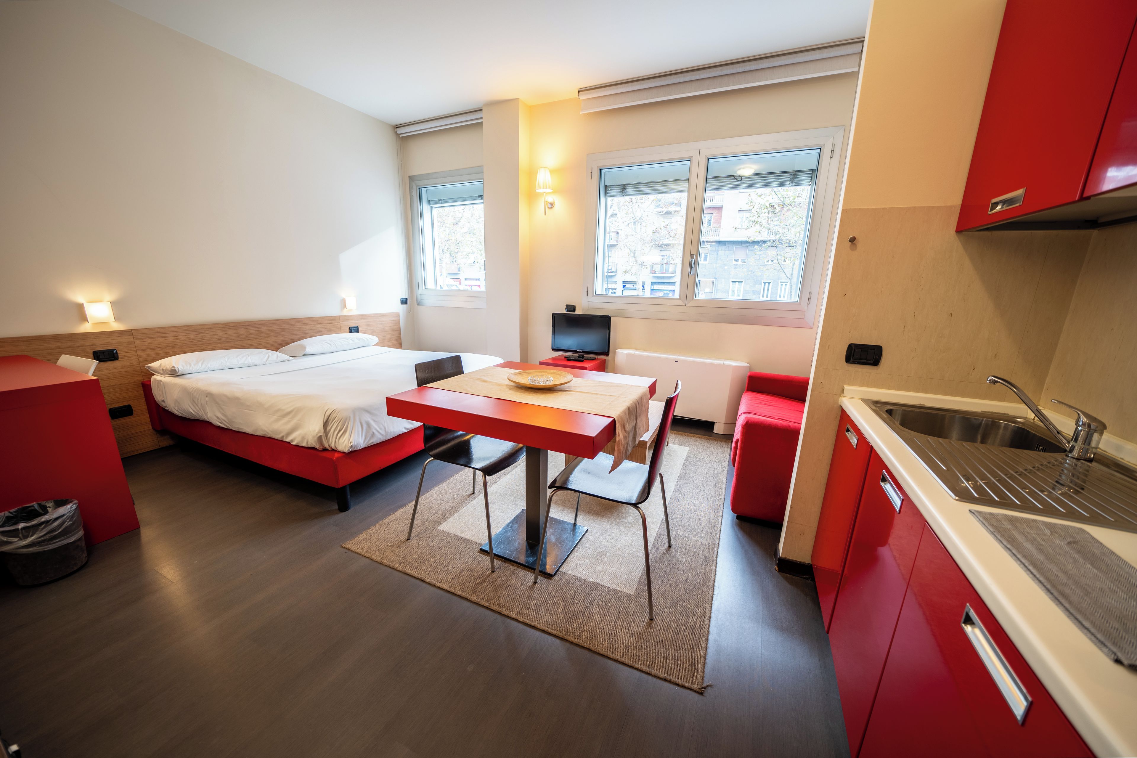 Habitación de hotel pequeña con cama, una mesita, escritorio, computadora y kitchenette.
