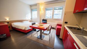 Habitación de hotel pequeña con cama, una mesita, escritorio, computadora y kitchenette.