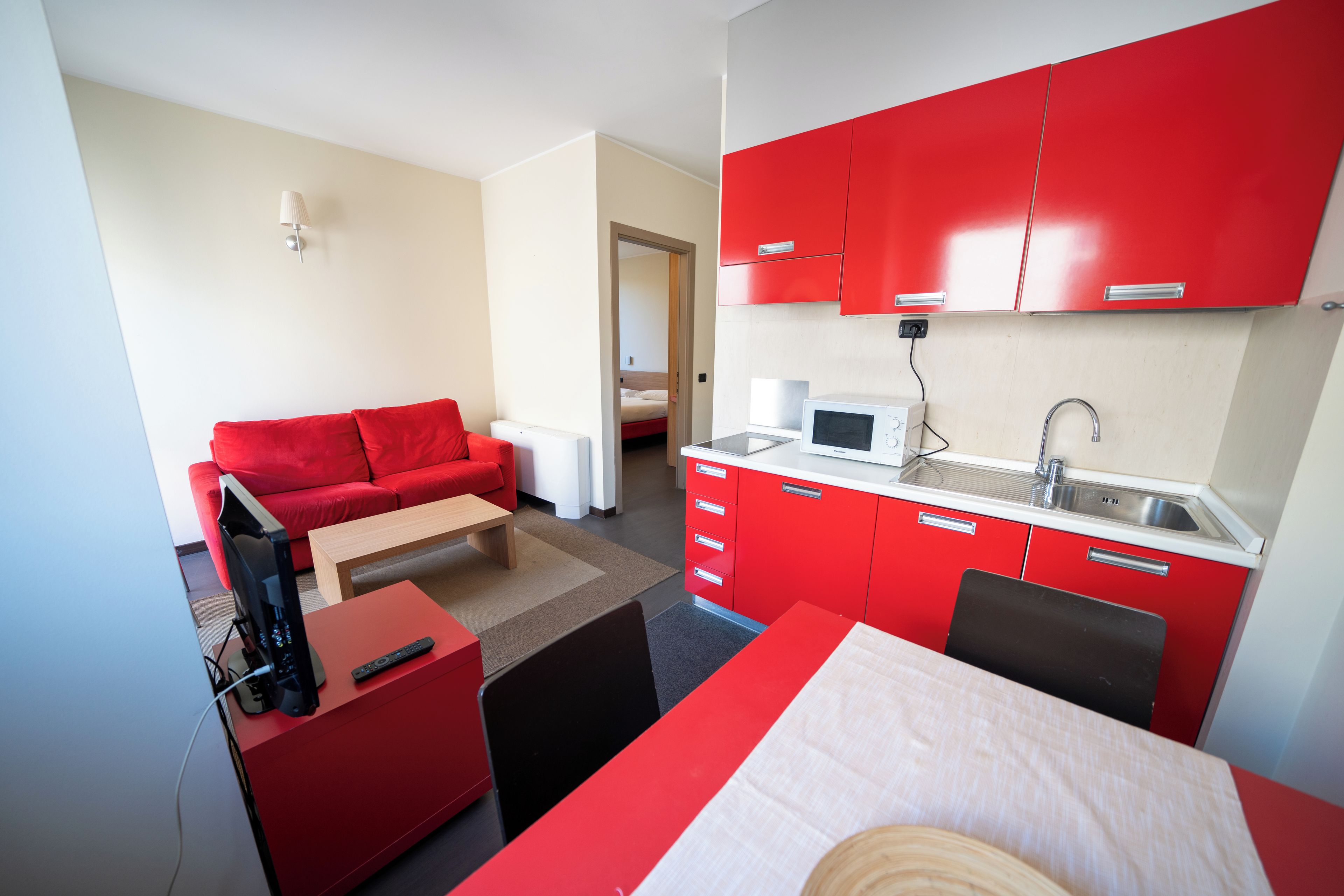 Un espace de vie compact comprenant un coin cuisine, un canapé rouge, un téléviseur et un coin repas.