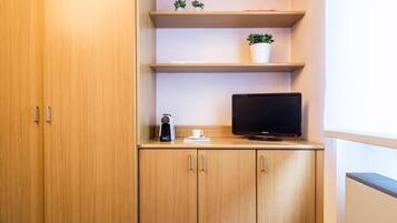 Un mueble de madera con un televisor de pantalla plana, una cafetera y dos plantas en macetas sobre estantes.
