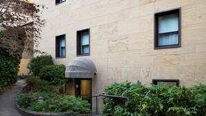 A modern building with a stone facade, a covered entrance, and a small garden area with plants and a pathway. - Residence Portello (Milan)