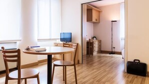 A modern, well-lit room with a round wooden table, two chairs, a television, and a kitchen area visible through an open door. - Residence Portello (Milan)
