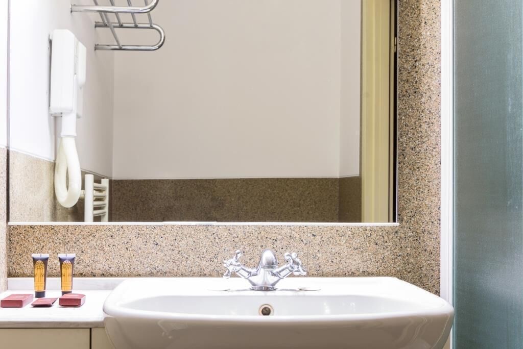 Une salle de bain avec un comptoir en granit, un lavabo blanc avec un robinet chromé et un miroir au-dessus du lavabo.