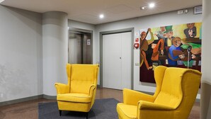 A hallway with two yellow armchairs, a door, and a painting on the wall. - Residence Portello (Milan)