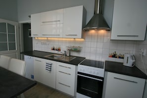A modern kitchen with white cabinets, a black countertop, a built-in oven, and a stainless steel range hood. - Apartment No. 4B I. P. Pavlova 32 (Karlovy Vary)