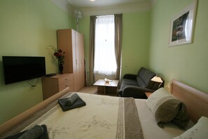 A hotel room with a bed, a TV, a desk, a sofa, and a window with curtains. - Apartment No. 4B I. P. Pavlova 32 (Karlovy Vary)