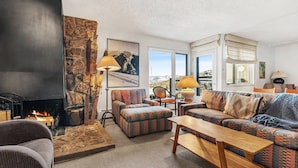 Una sala de estar acogedora con chimenea, sofá estampado y vistas a las montañas.