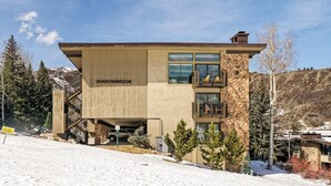 Un edificio de dos pisos llamado Shadowbrook, con fachada de piedra, ventanas grandes y un balcón con mobiliario exterior.