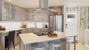 Una cocina moderna con una isla central, electrodomésticos de acero inoxidable y un detalle decorativo en la pared.