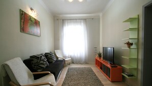 A living room with a sofa, armchair, TV, and a green shelf unit. - Apartment No. 21 I. P. Pavlova 34 (Karlovy Vary)