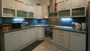 A modern kitchen with white cabinets, a built-in oven, a microwave, and a stainless steel range hood. - Apartment No. 21 I. P. Pavlova 34 (Karlovy Vary)