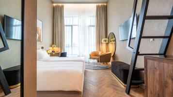 Une chambre d’hôtel avec un grand lit, un bureau avec une chaise, un téléviseur fixé au mur et une fenêtre avec des rideaux.