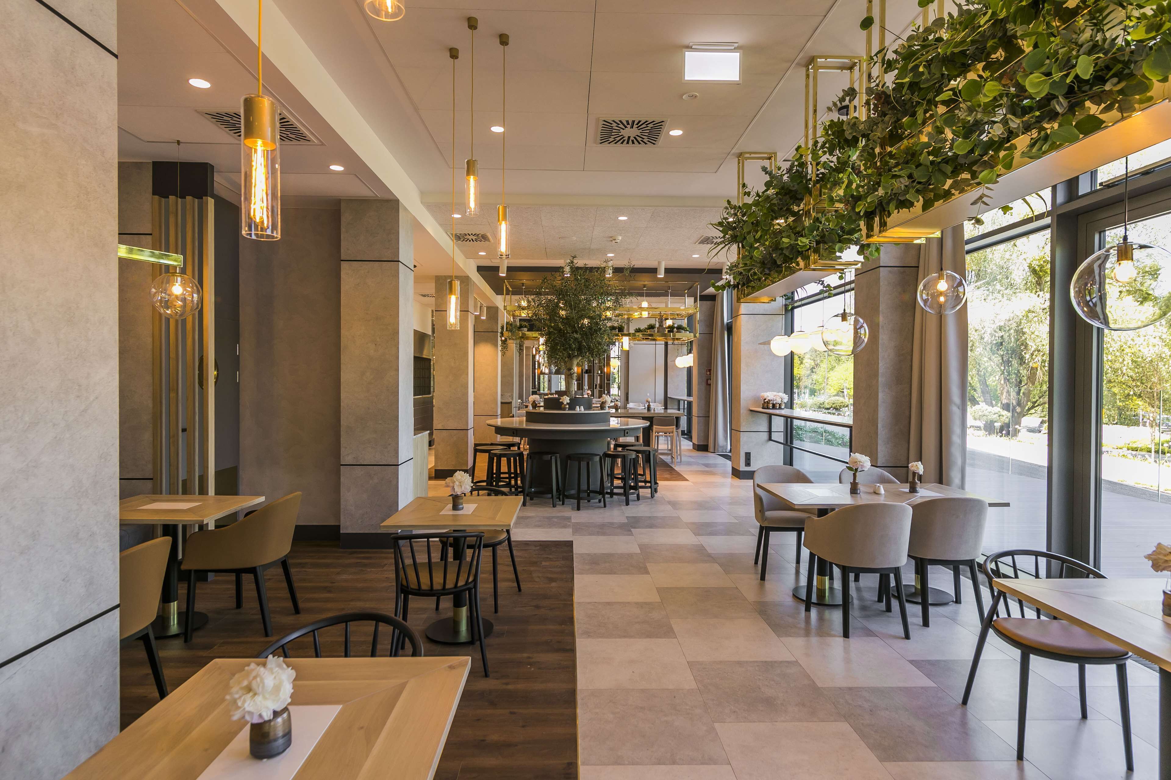 A modern restaurant with a central bar, seating arrangements, and large windows offering natural light.