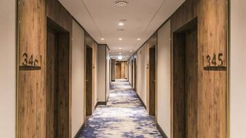 A hotel hallway with wooden paneling and numbered doors, leading to rooms.