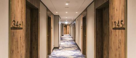 A hotel hallway with wooden paneling and numbered doors, leading to rooms.