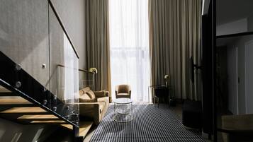 Una sala de estar moderna con una escalera, un sofá, una mesa de centro y vistas a través de cortinas translúcidas.