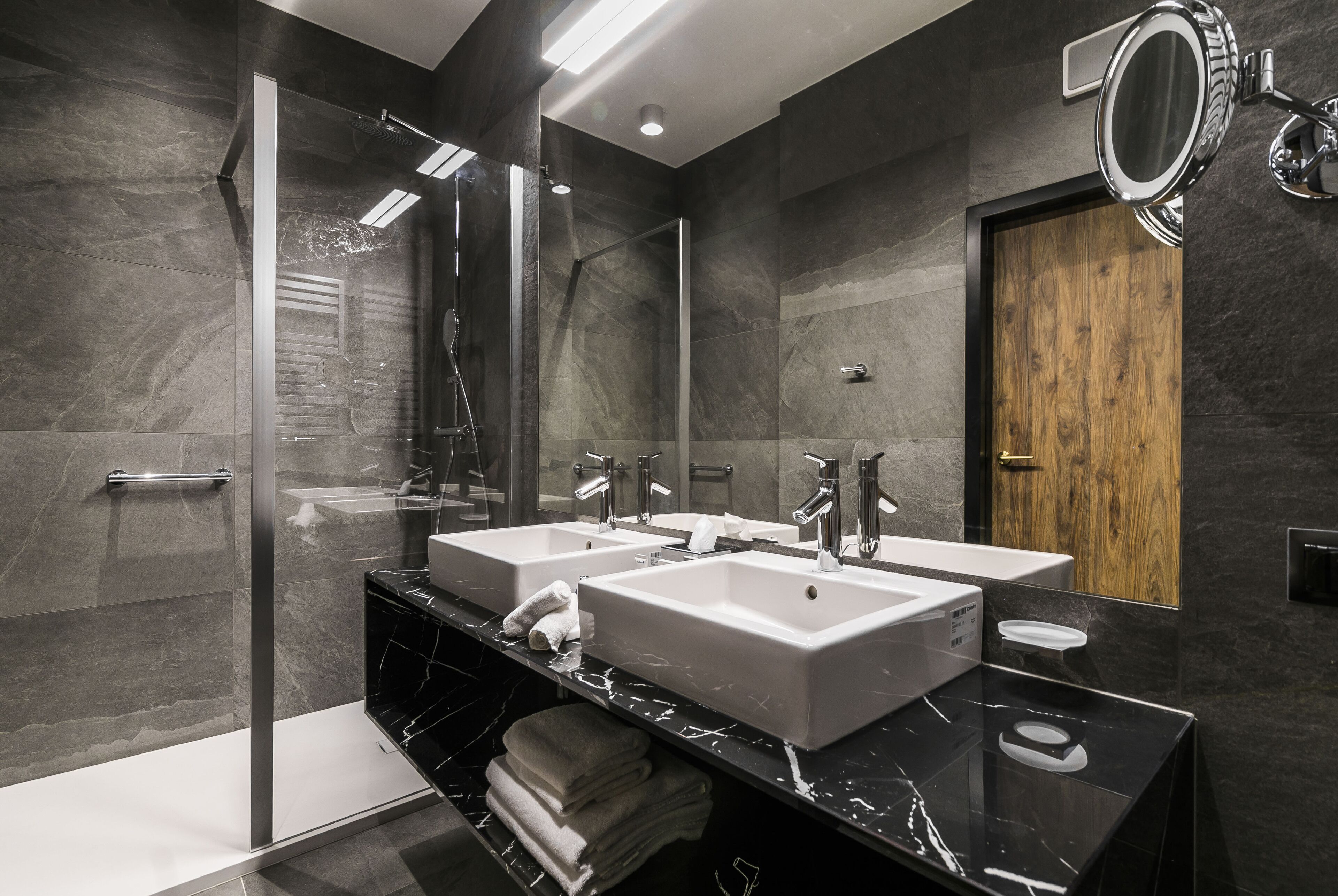 A modern bathroom with two sinks, a glass shower enclosure, and a wooden door.