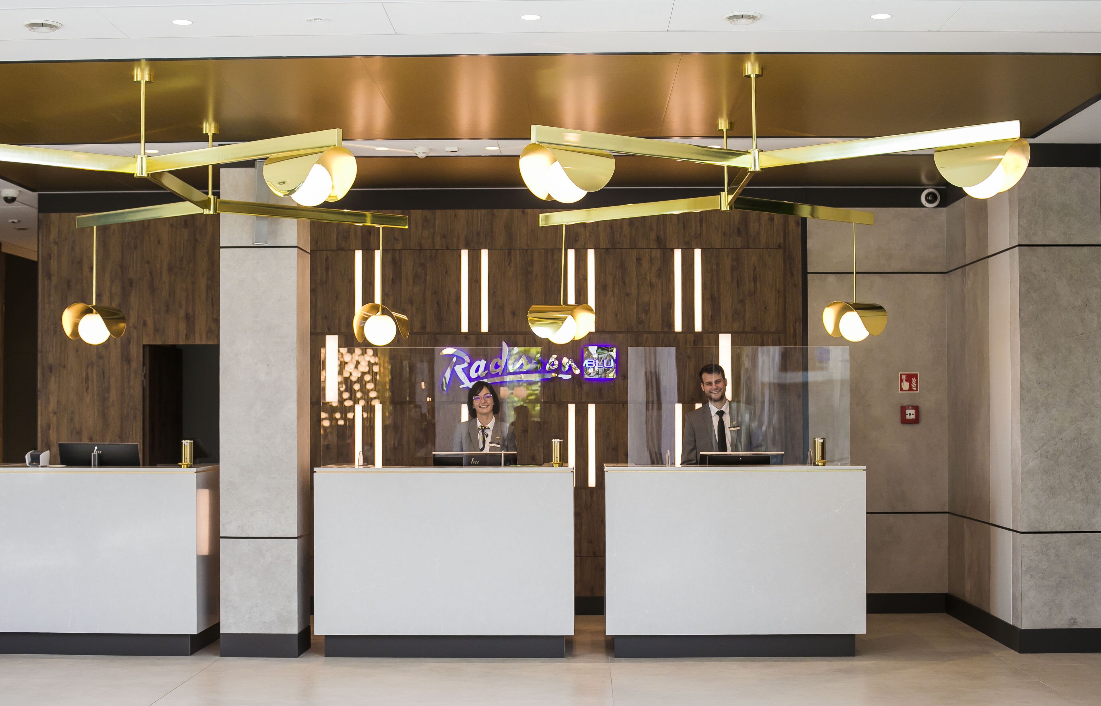 A reception area with three white reception desks, modern pendant lighting, and a neon sign in the background.