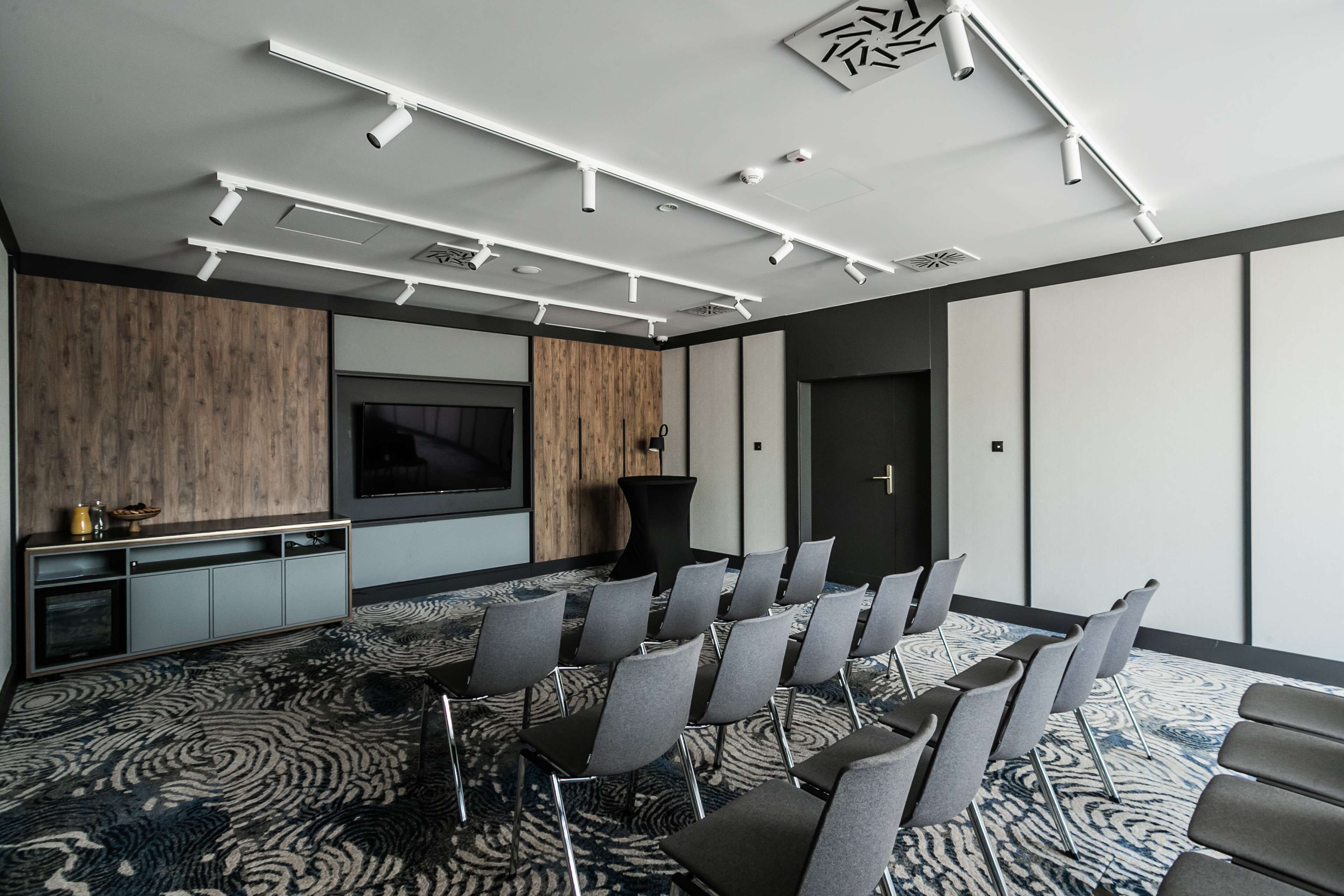 A conference room with a large screen, rows of chairs, and a patterned carpet.