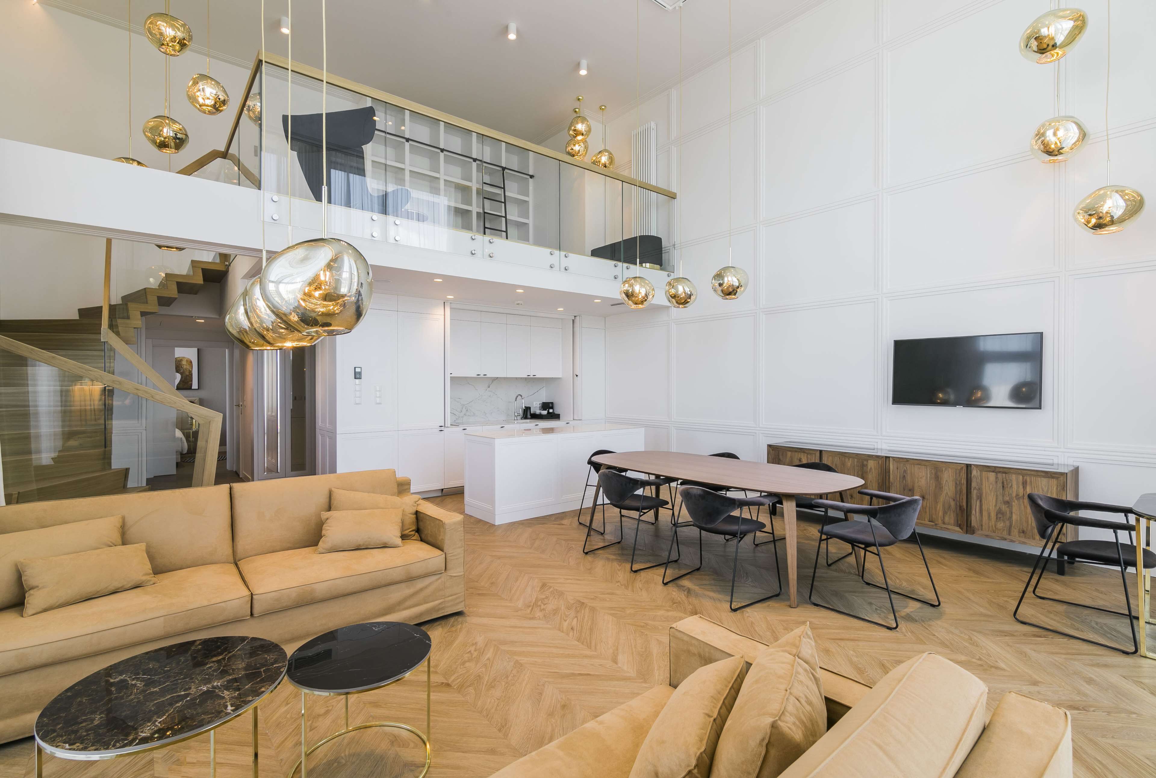 A spacious living area with a sofa, coffee table, and dining table. A staircase leads to an upper level with a balcony.