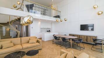 A spacious living area with a sofa, coffee table, and dining table. A staircase leads to an upper level with a balcony.