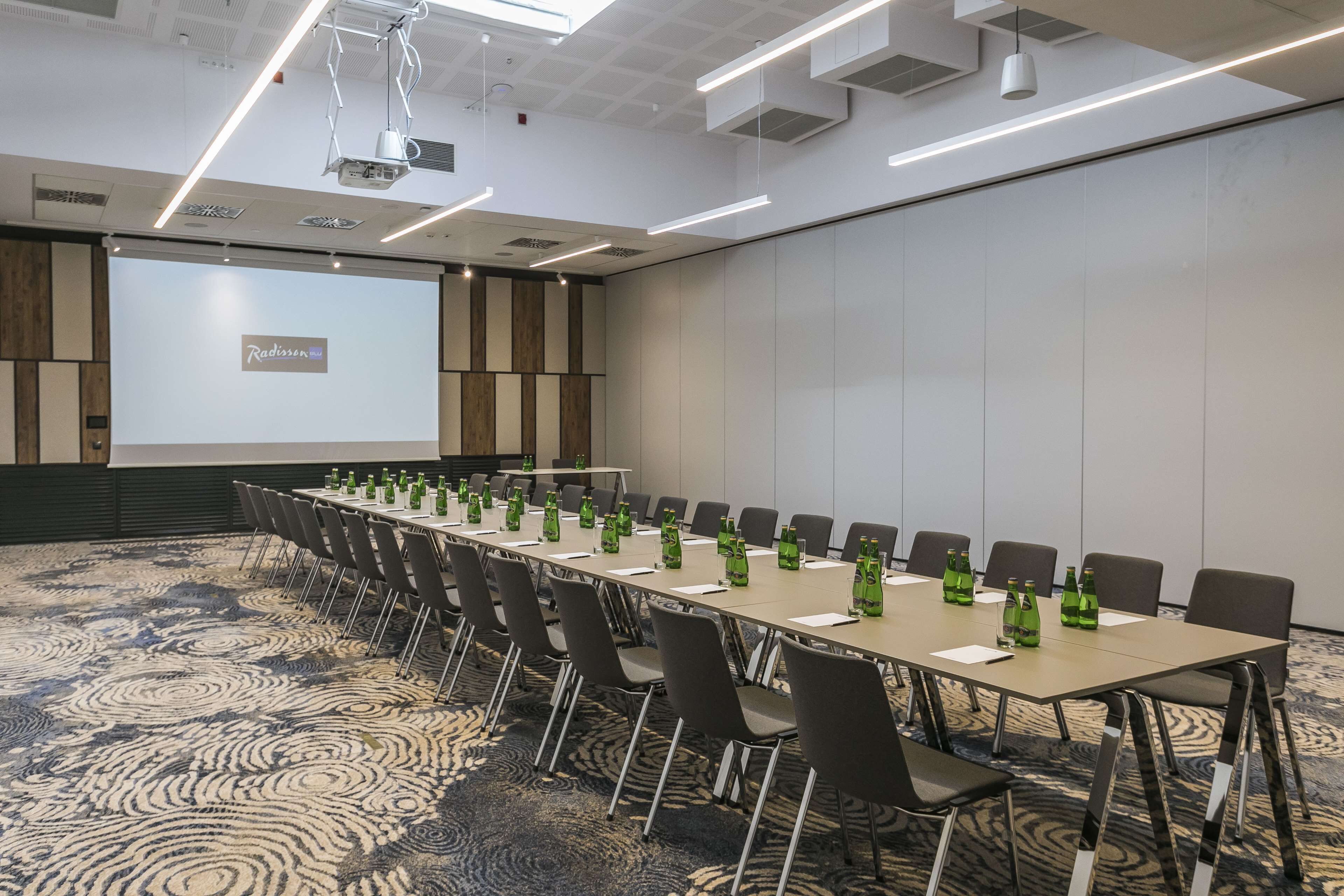 Een congreszaal met een lange tafel, stoelen en een projectiescherm waarop 'Radisson' staat.