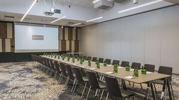 Een congreszaal met een lange tafel, stoelen en een projectiescherm waarop 'Radisson' staat.