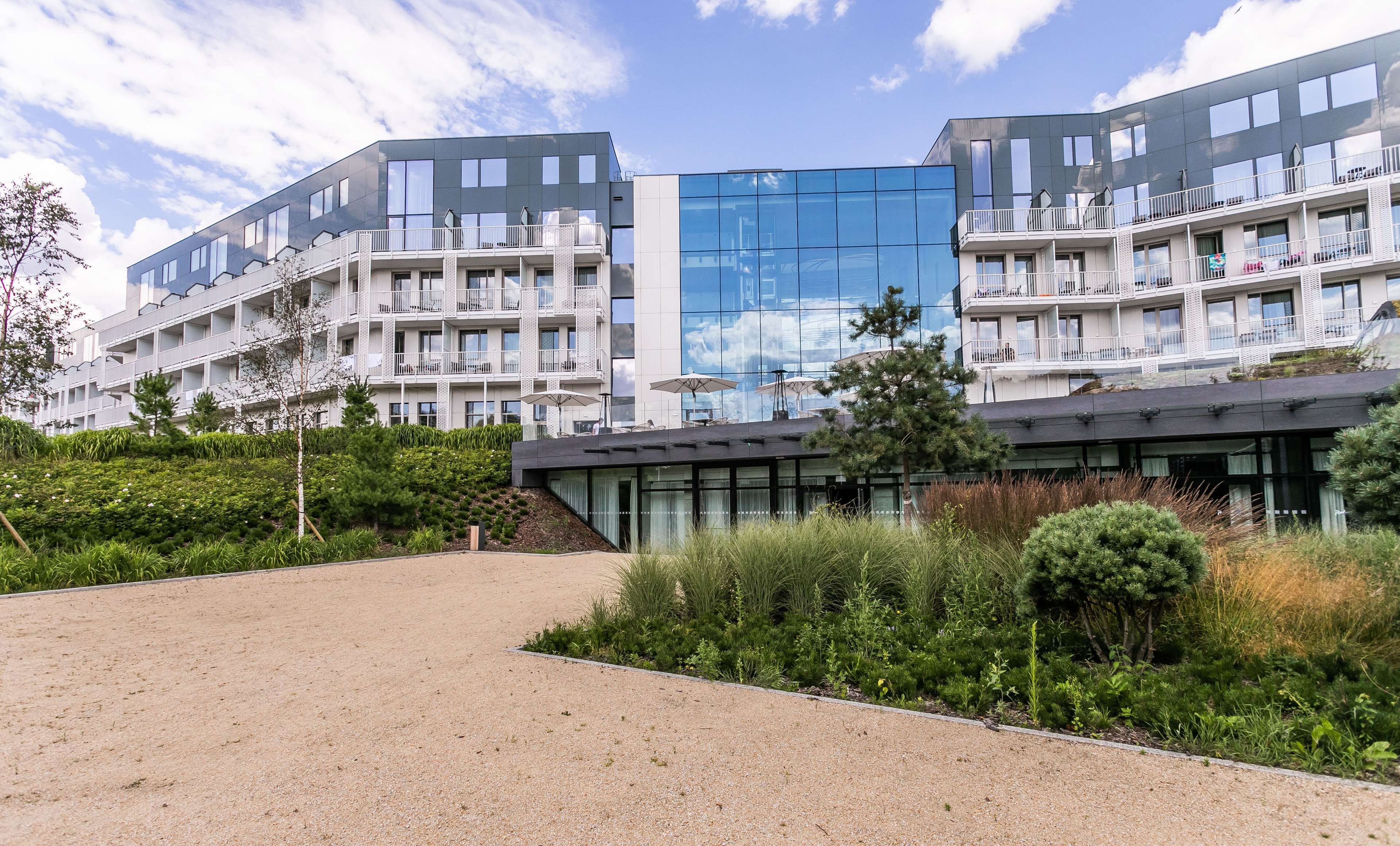 Ein modernes Apartmenthaus mit Balkonen, einer reflektierenden Glasfassade und einer begrünten Außenanlage.