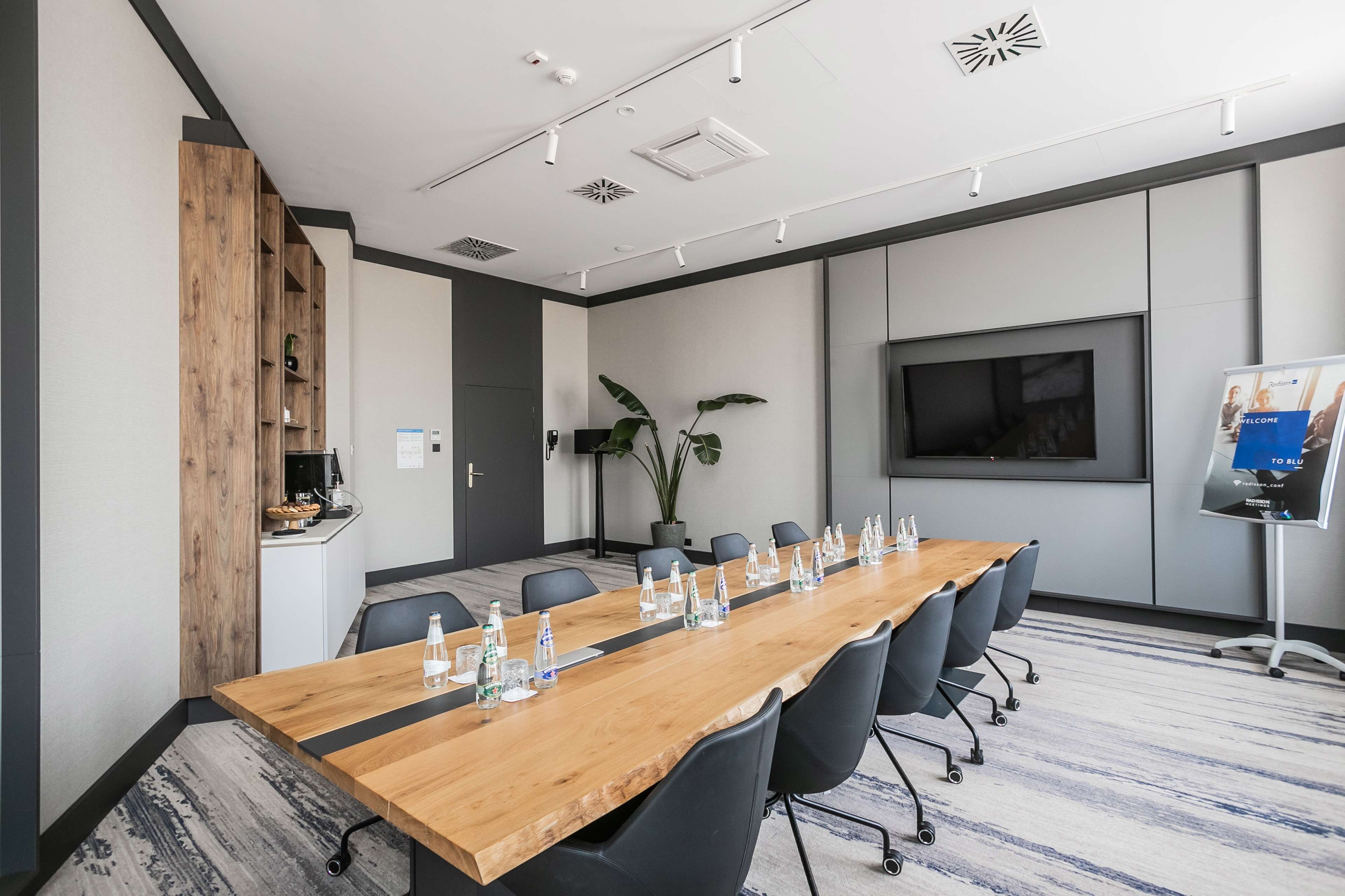 A conference room with a long wooden table, black chairs, a large screen, and a whiteboard.