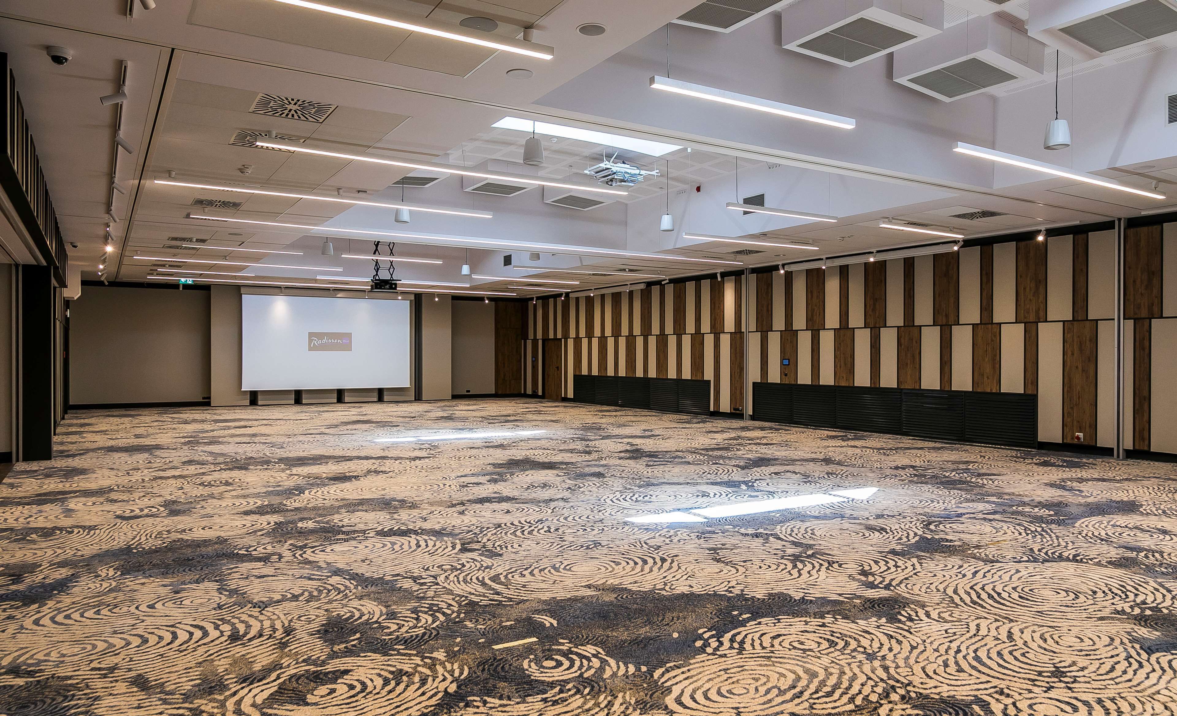 A large conference room with a patterned carpet, ceiling lights, and a projection screen.