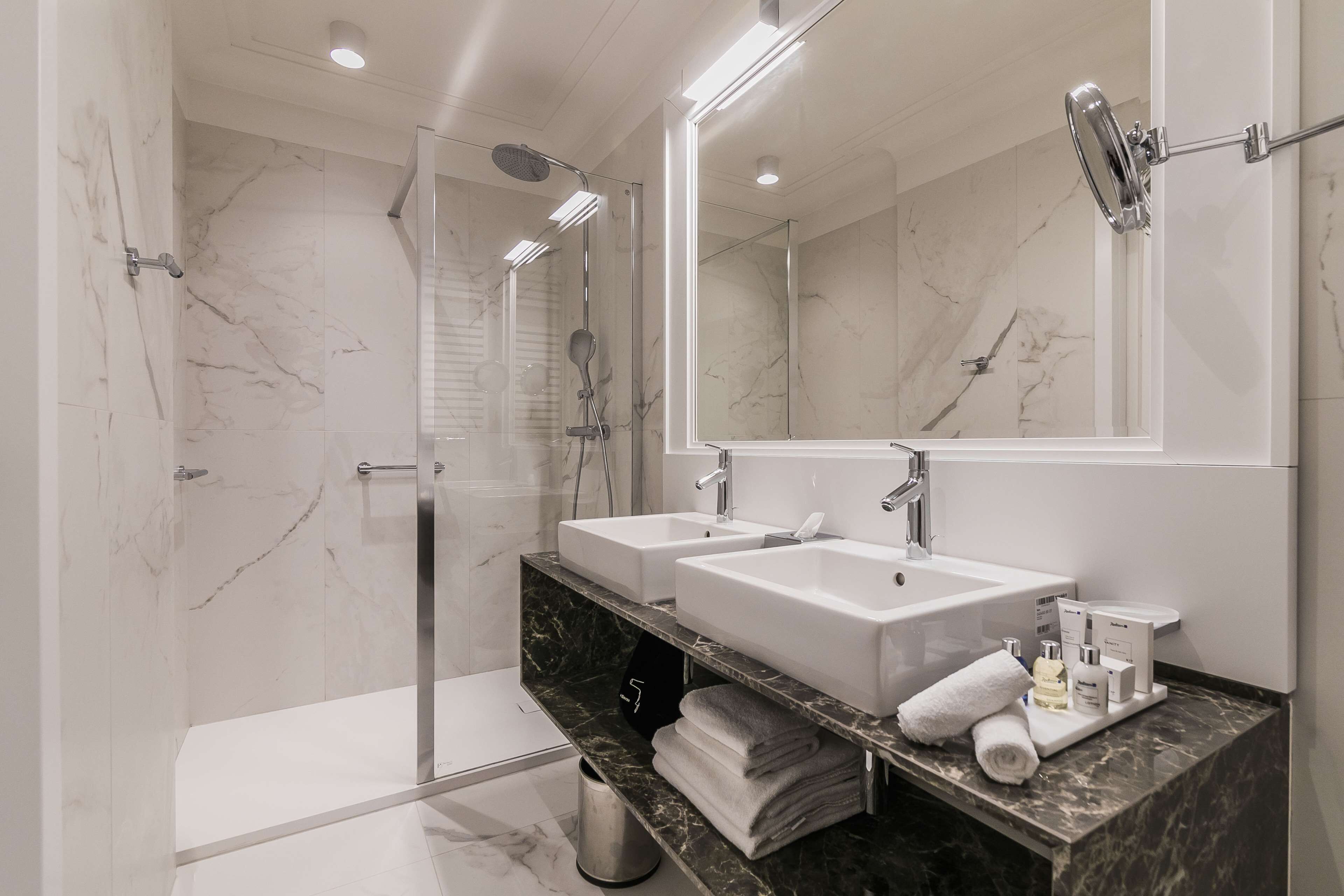 Une salle de bain moderne avec deux lavabos, un grand miroir et une douche à parois de verre.