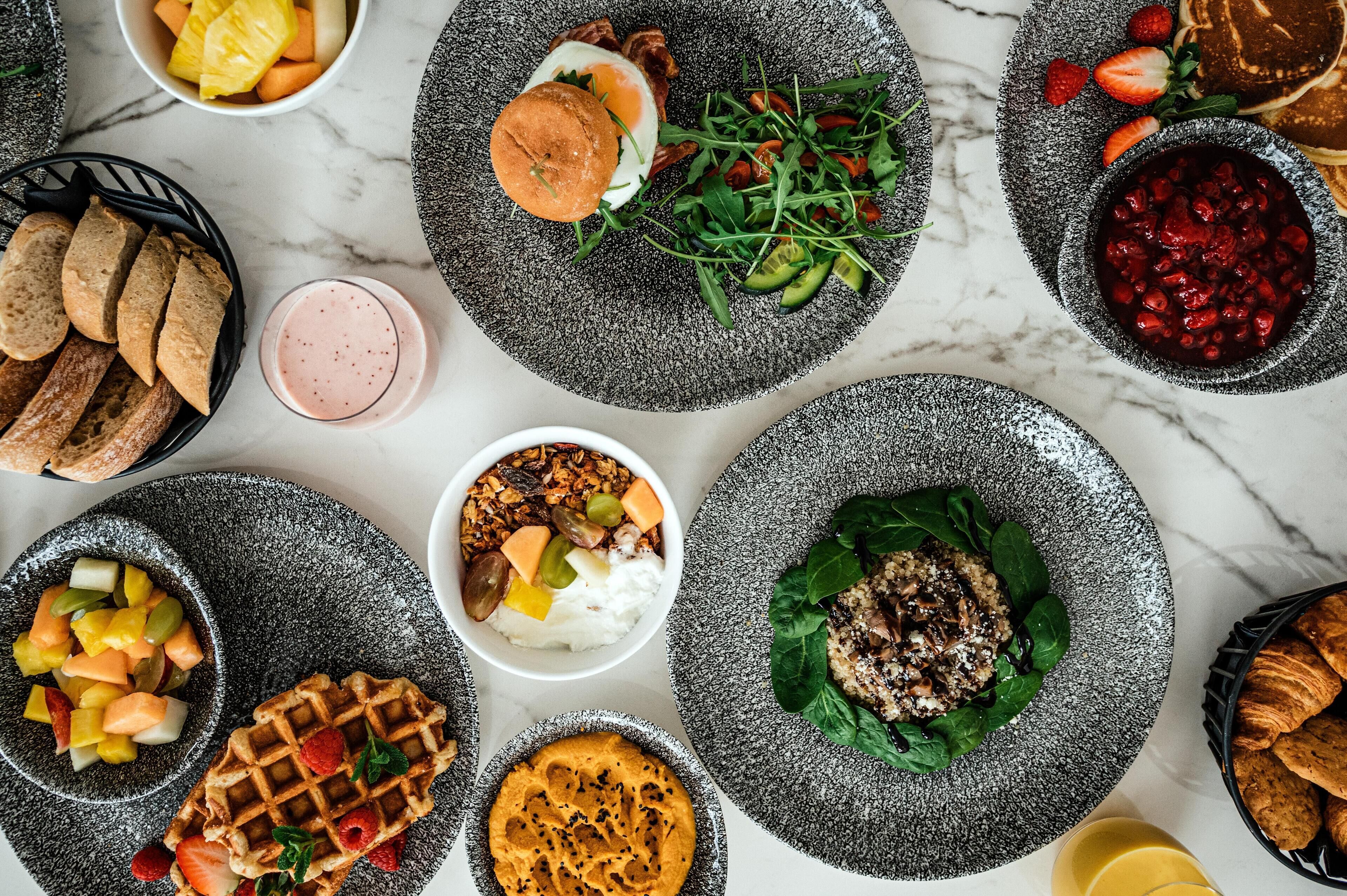 Une variété de plats, dont un hamburger, une salade et des gaufres, disposés sur une surface en marbre.