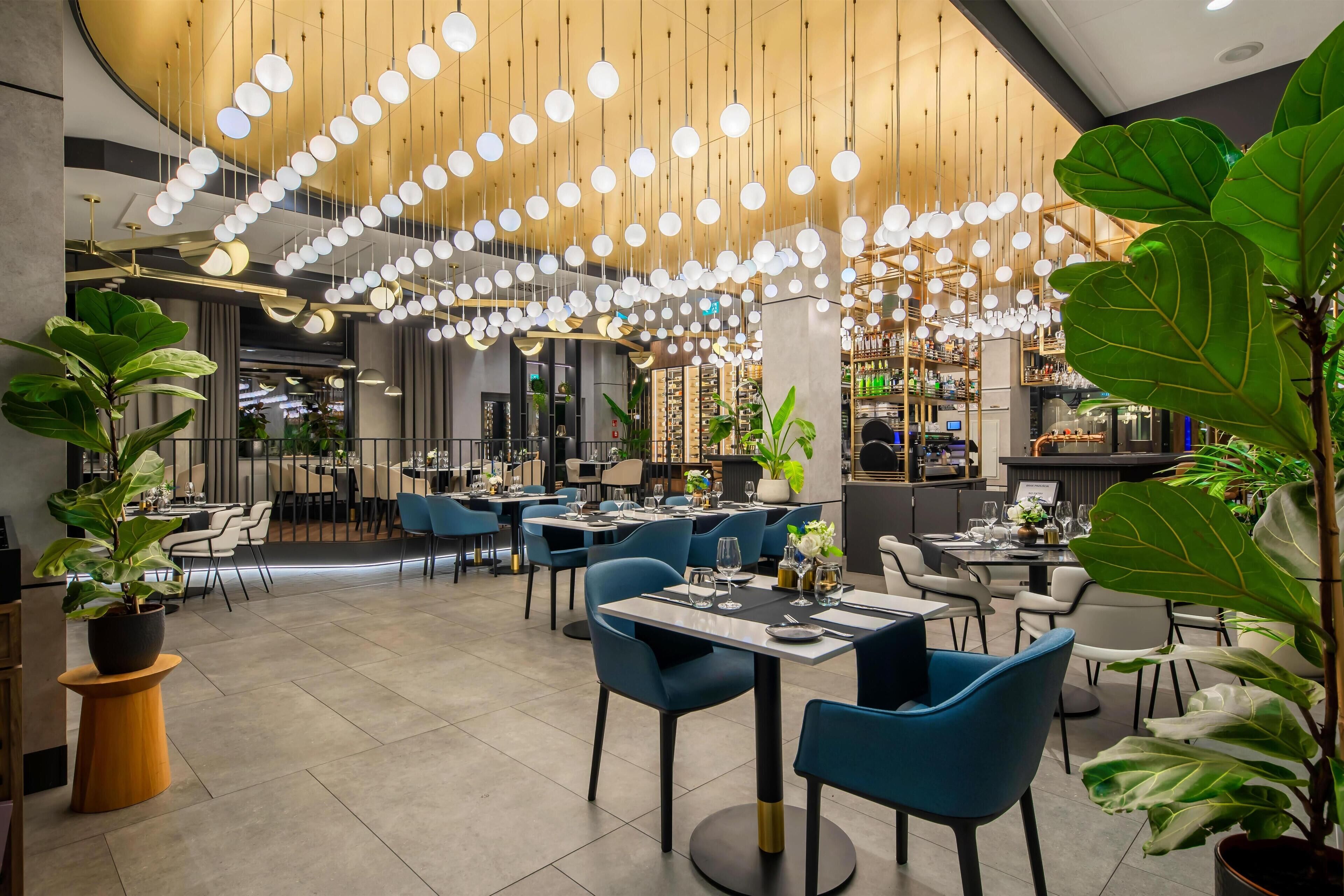 A modern restaurant interior with hanging spherical lights, blue chairs, and potted plants.