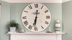 A large wall-mounted clock with Roman numerals and the text "Paris Standard Clock Company" on a light blue wall.