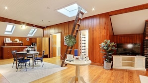 Un espacio habitable amplio con suelo de madera, una mesa de comedor con sillas, una escalera, un televisor y una planta grande.