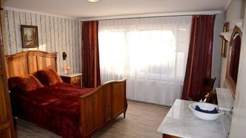 A bedroom with a wooden bed, a nightstand, a marble sink, and a large window with curtains.