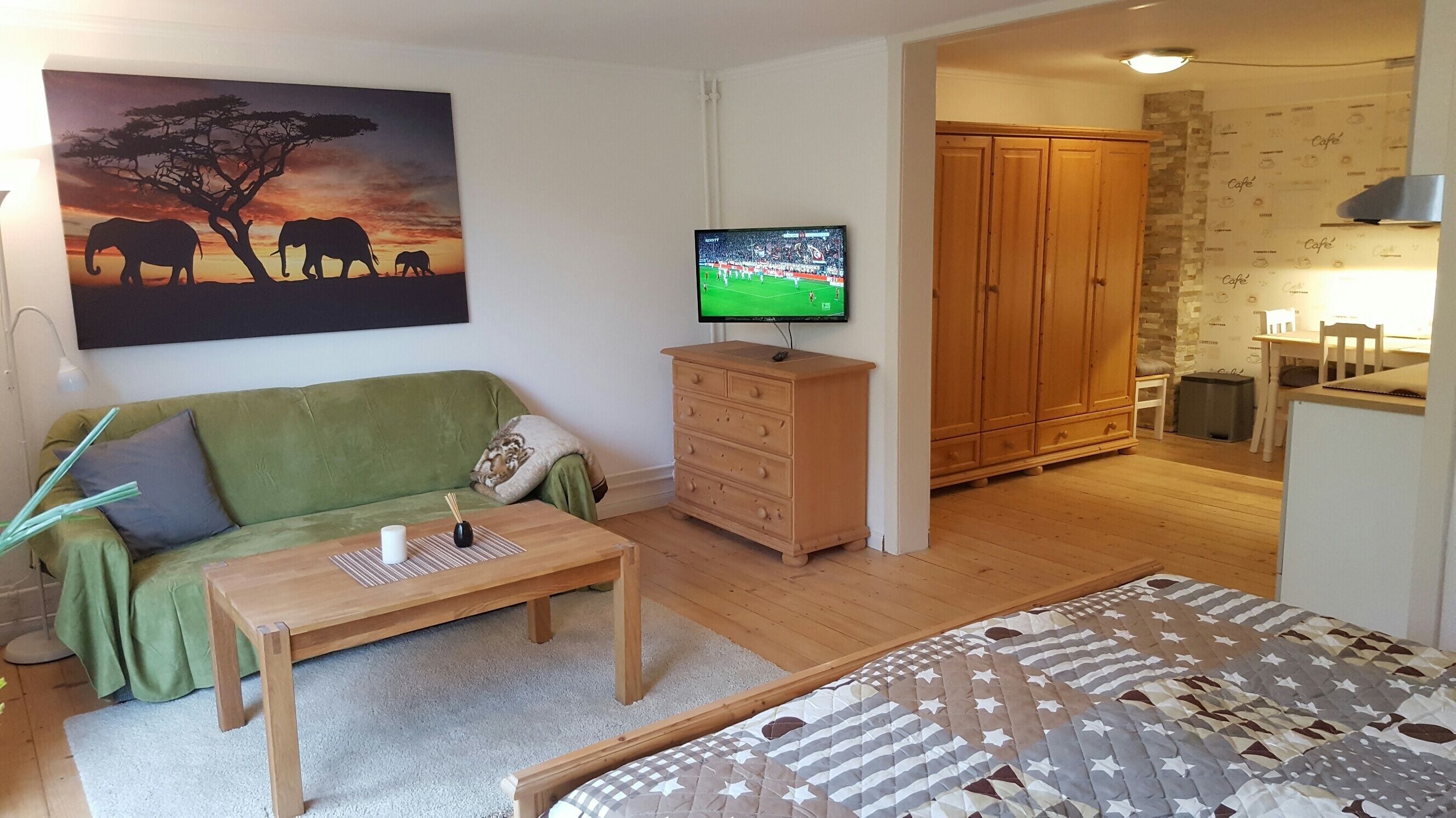 En stue med en grøn sofa, et træbord, et fjernsyn på et træskab og et billede af elefanter.
