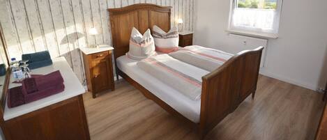 Une chambre avec un lit en bois, des tables de chevet, une commode, une fenêtre donnant sur un beau paysage et un plancher en bois.