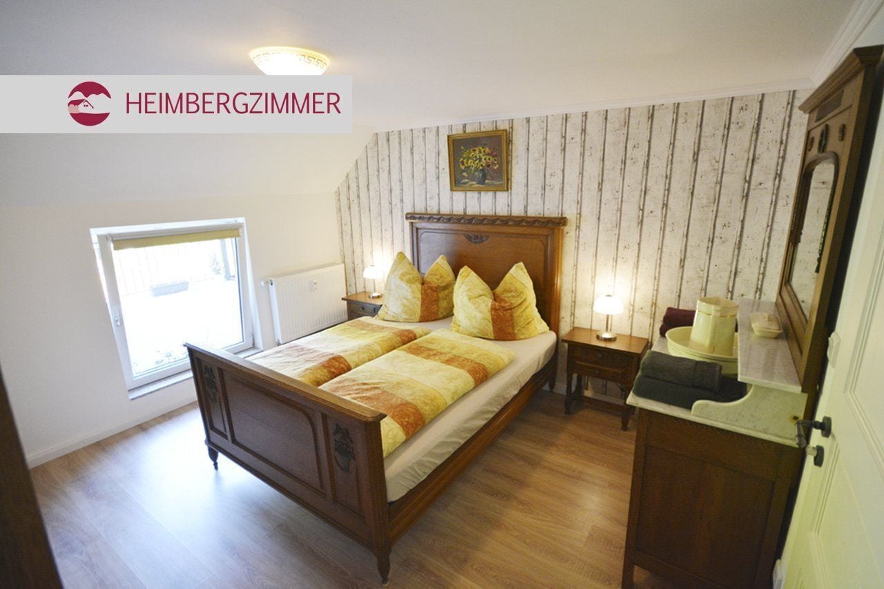 A bedroom with a wooden bed, a nightstand, a bedside table, a window, and a mirror.