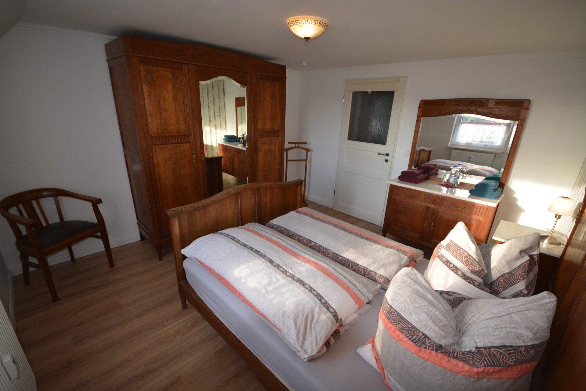 Ein Schlafzimmer mit einem hölzernen Bett, einem Schrank aus Holz, einem Spiegel, einem Stuhl und einem Badezimmer mit Waschbecken und Spiegel.