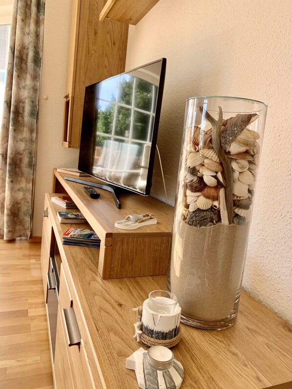 A wooden TV stand with a flat-screen TV, a glass vase with seashells, and a candle holder. - Reethaus Boddenblick in Alt Reddevitz with parking lot, ground-level terrace, Wgh12 (Alt Reddevitz)