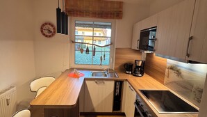 A compact kitchen with a wooden countertop, a built-in oven, a microwave, and a window with a view of a house. - Reethaus Boddenblick in Alt Reddevitz with parking lot, ground-level terrace, Wgh12 (Alt Reddevitz)