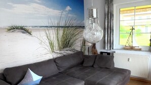 A modern living room with a grey sectional sofa, a glass coffee table, and a beach-themed wall mural. - Reethaus Boddenblick in Alt Reddevitz with parking lot, ground-level terrace, Wgh12 (Alt Reddevitz)