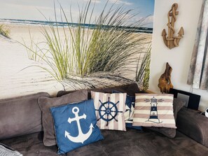 Uma sala de estar com tema praiano, incluindo um sofá, almofadas decorativas e um mural na parede.