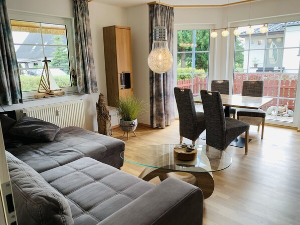 A modern living room with a glass coffee table, grey sofas, and a dining area with wicker chairs. - Reethaus Boddenblick in Alt Reddevitz with parking lot, ground-level terrace, Wgh12 (Alt Reddevitz)