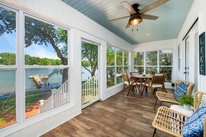 A covered patio with large windows overlooking a lake, wooden flooring, and wicker furniture. - Summer STATus w/Optional Boat Rental (Mooresville)