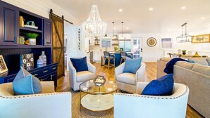 A spacious living room with a chandelier, white sofas with blue cushions, and a dining area in the background. - Summer STATus w/Optional Boat Rental (Mooresville)