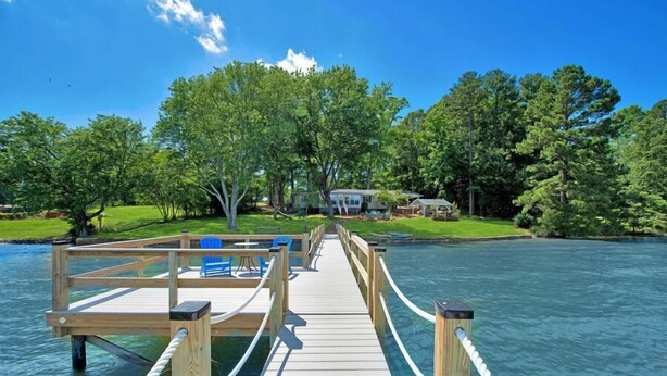 A wooden pier leading to a dock with blue chairs and a small house in the background. - Summer STATus w/Optional Boat Rental (Mooresville)
