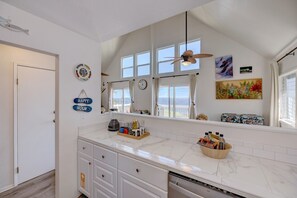 A kitchen with a large island, a ceiling fan, and a view of the ocean through the windows.