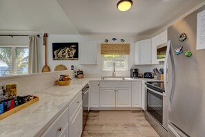 A modern kitchen with white cabinets, a stainless steel refrigerator, a microwave, and a coffee maker.